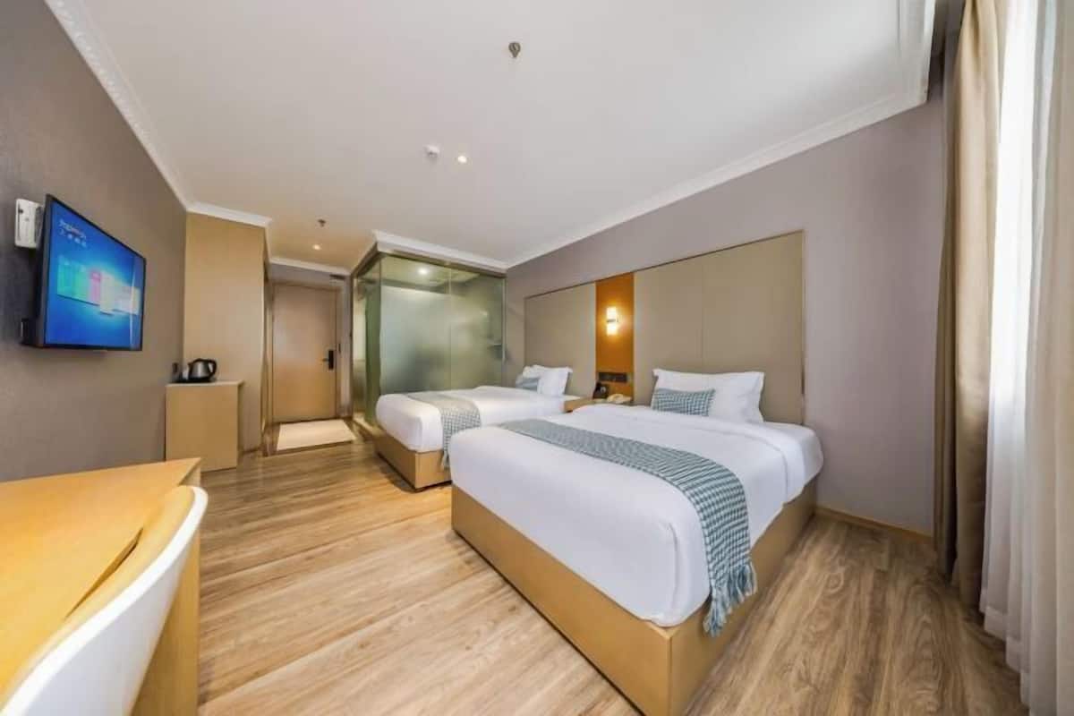 Une chambre d’hôtel avec deux lits, un bureau, une télévision et une cloison en verre.