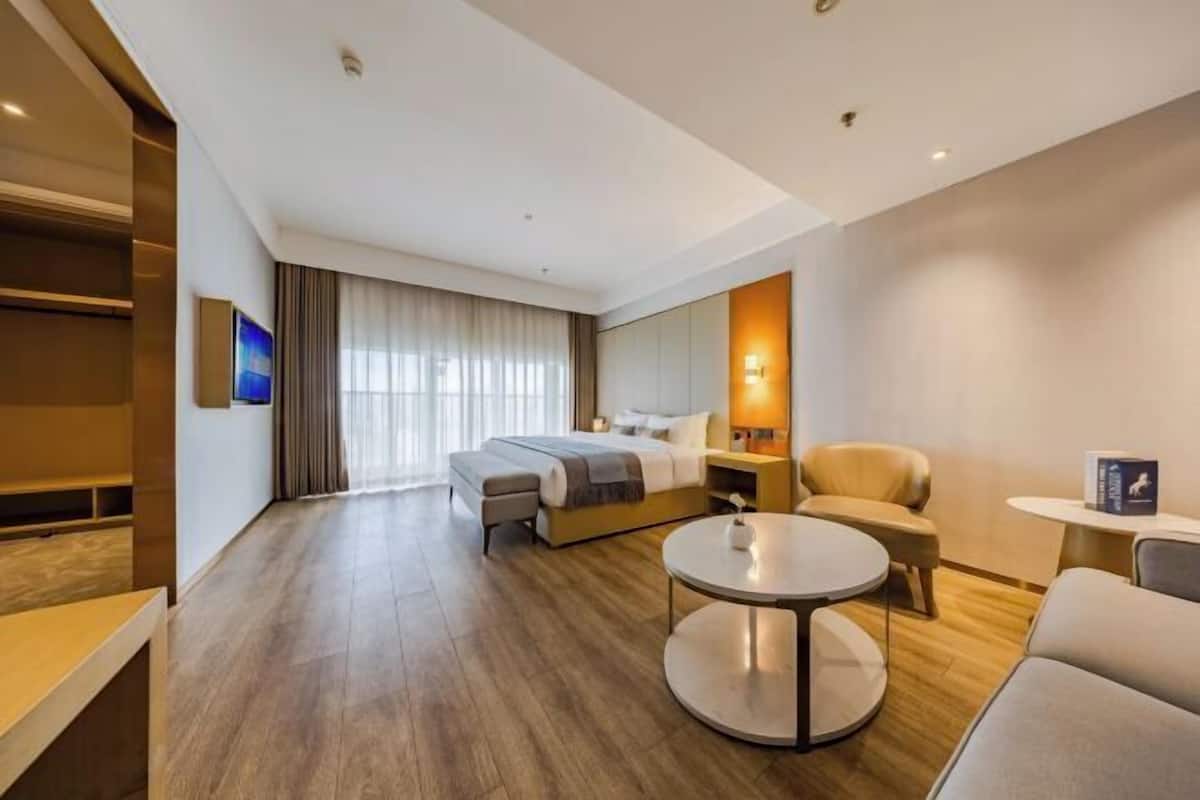 Une chambre d’hôtel moderne équipée d’un lit, d’un coin salon avec une table ronde et d’un téléviseur fixé au mur.