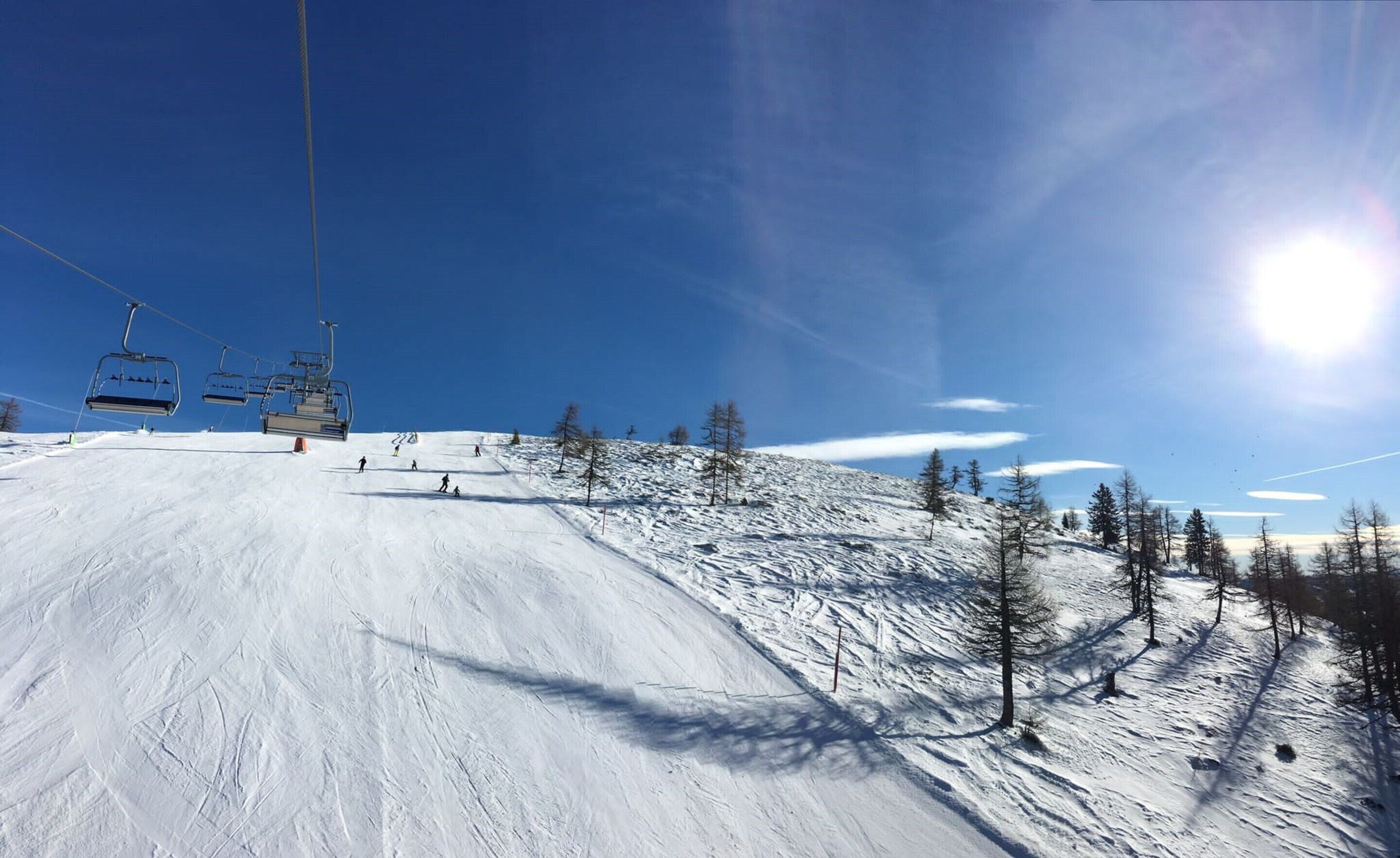A ski slope with a ski lift, trees, and a clear blue sky.