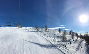 A ski slope with a ski lift, trees, and a clear blue sky.