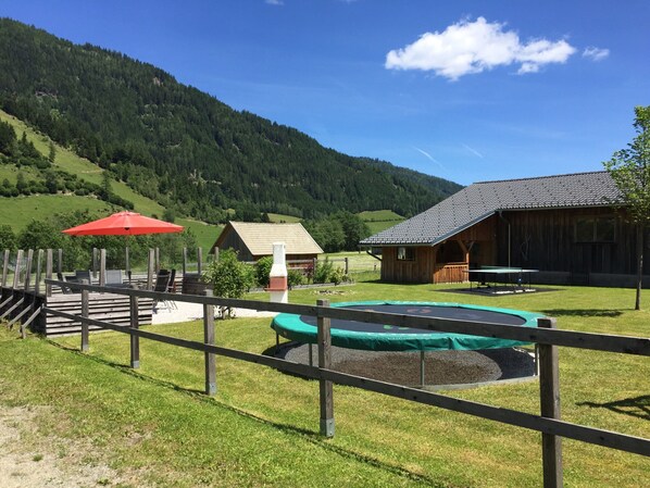 A wooden cabin with a dining area, a trampoline, and a red umbrella.