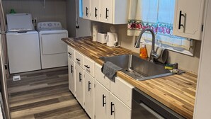 Una cocina compacta con armarios blancos, encimera de madera y pileta de acero inoxidable.