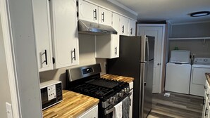 Una cocina compacta con armarios blancos, una estufa negra, un refrigerador de acero inoxidable y un microondas.