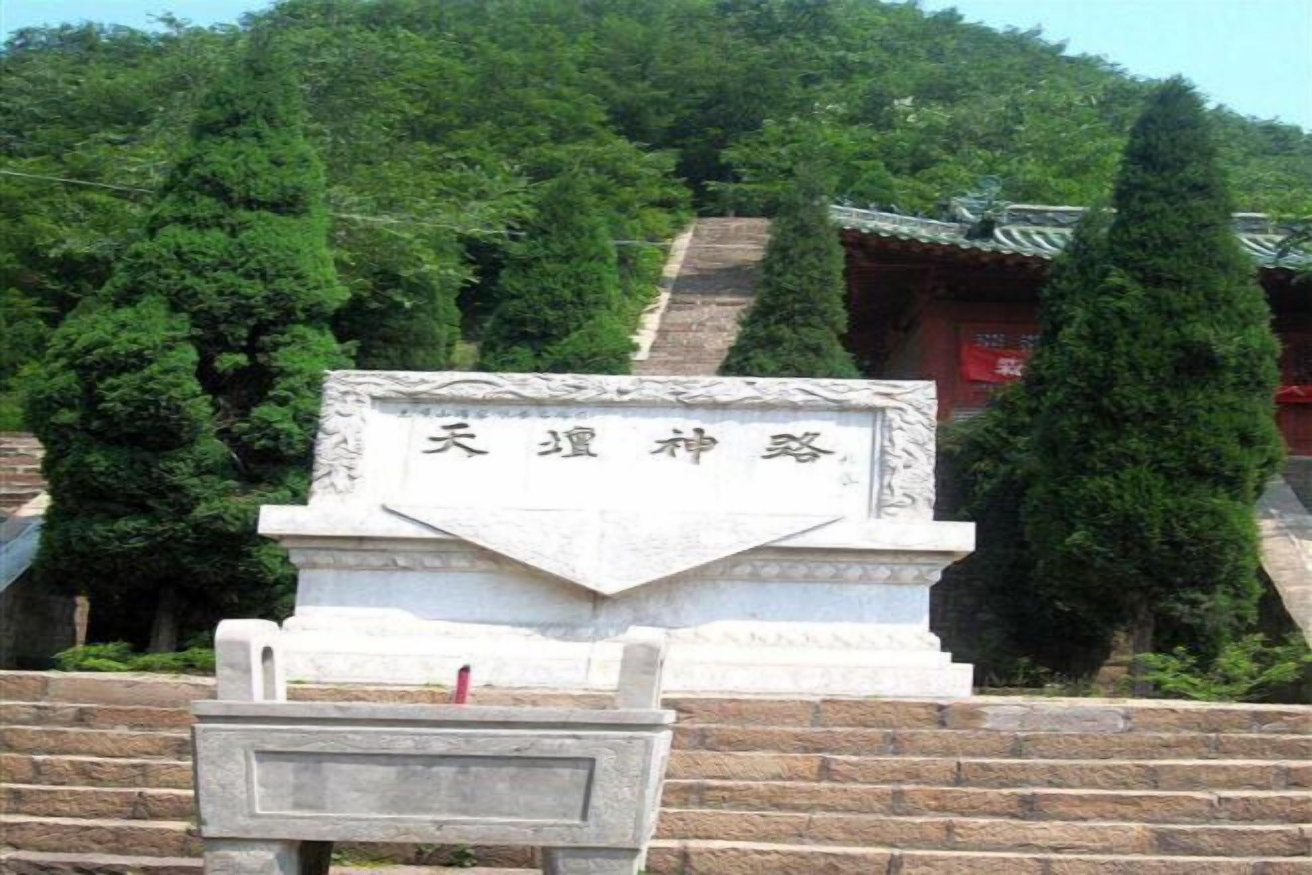 A stone monument with inscriptions, a staircase, and a traditional building with a tiled roof in the background.