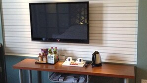 A flat-screen TV mounted on a wall above a wooden table with a tray of breakfast items, including a kettle and condiments. - Light Living City Preferred Hotel (RT-Mart) (Jiyuan)