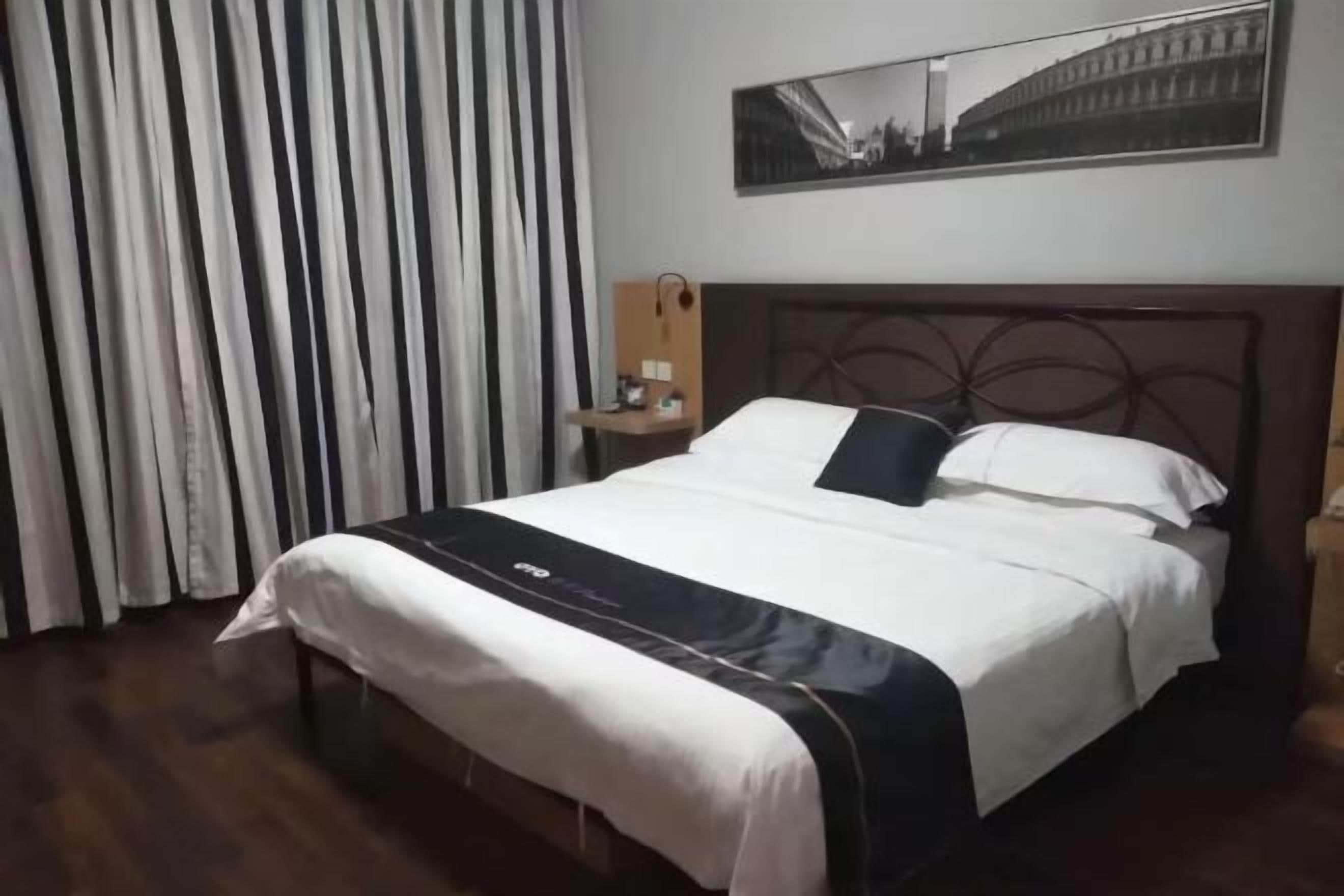 Hotellihuone, jossa on sänky, yöpöytä, peili ja seinällä oleva kehystetty kuva.