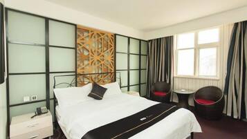 Una habitación de hotel con cama, mesita de noche, silla y ventana con cortinas.