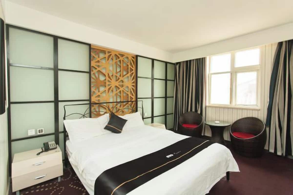 A hotel room with a bed, bedside table, chair, and a decorative wall panel.