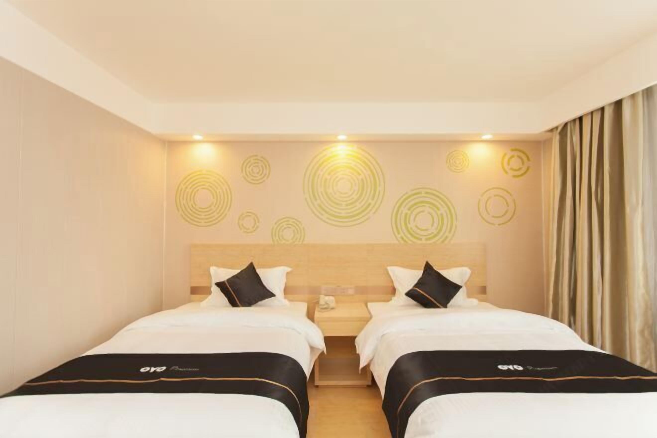 Une chambre d’hôtel avec deux lits, une tête de lit en bois, un mur orné de motifs circulaires et un rideau sur le côté droit.