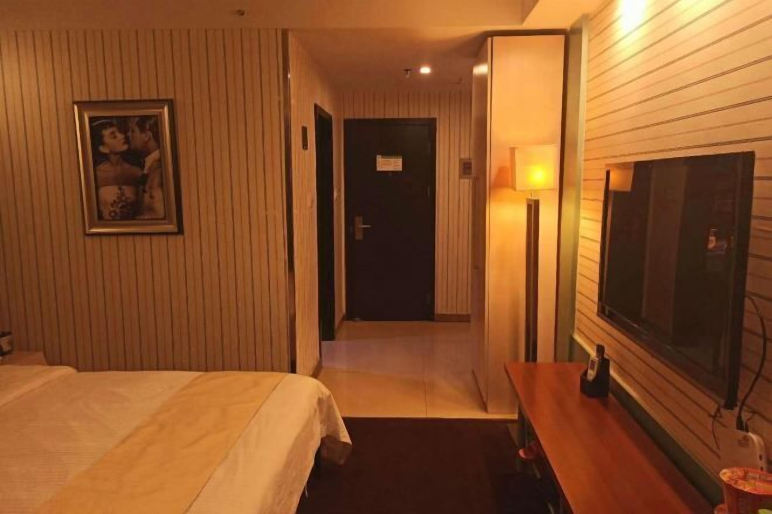 A hotel room with a bed, a desk, a TV, and a door leading to another room.