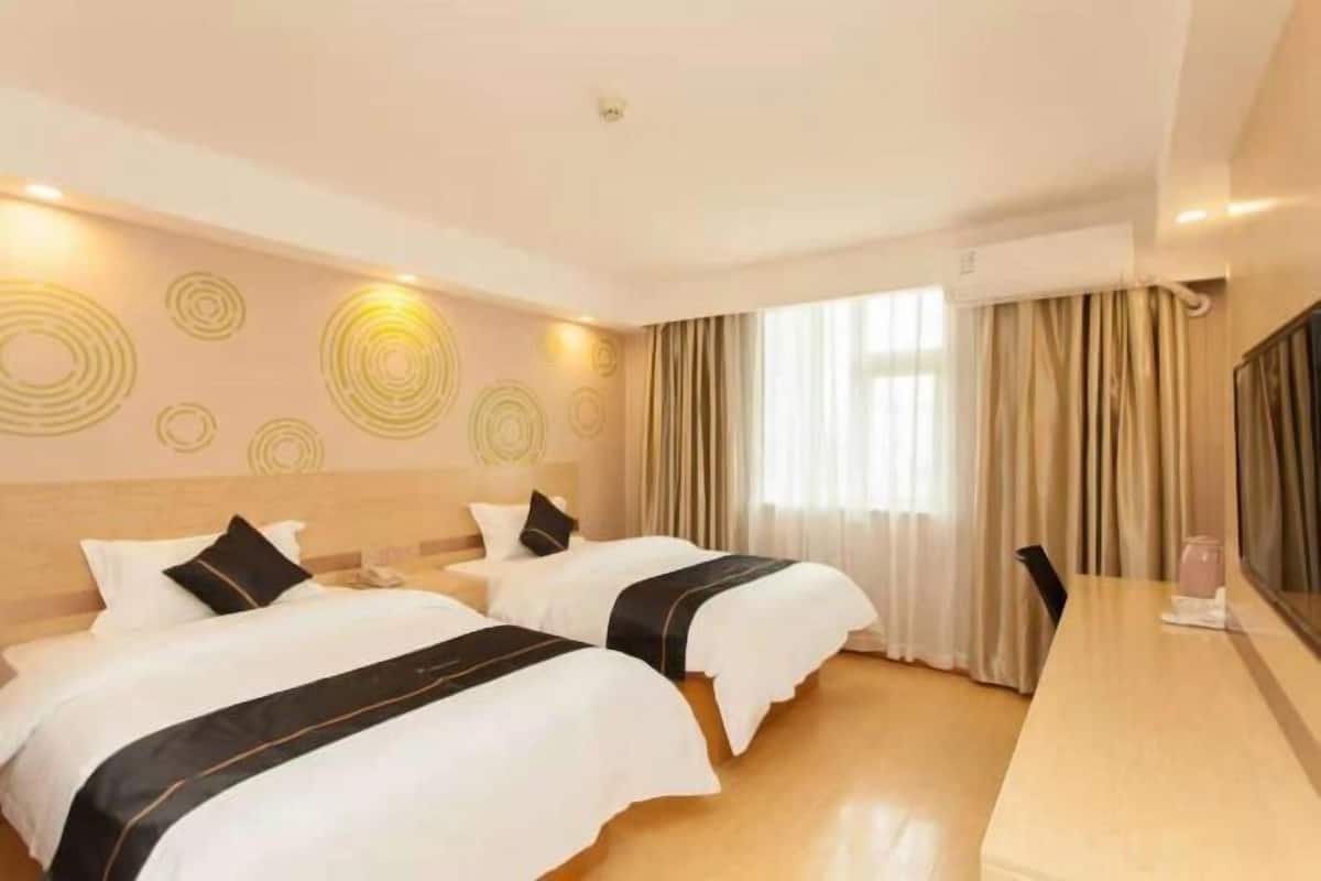 A hotel room with two beds, a large window with curtains, a wooden floor, and a long table.