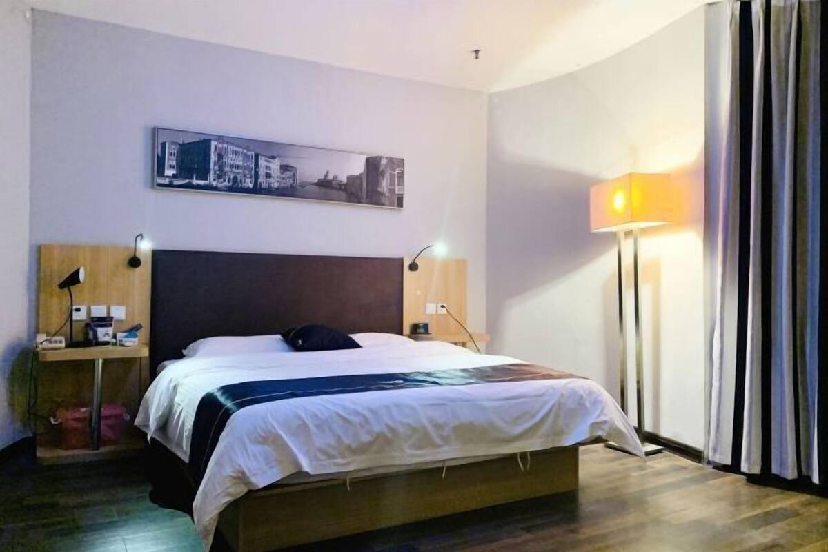 A hotel room with a bed, bedside lamps, a nightstand, a lamp, a picture on the wall, and a curtain.