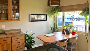 A kitchen with wooden cabinets, a dining table, chairs, a hanging plant, and a window with a view of the street. - Central Encinitas, 1.4 Miles from Beach (Encinitas)