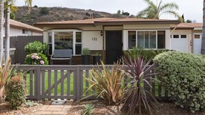A single-story house with a number 733 on the door, a small porch with a chair, and a fenced yard with various plants. - Central Encinitas, 1.4 Miles from Beach (Encinitas)