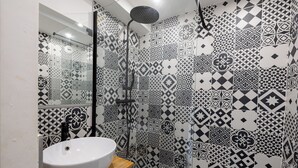 A bathroom with a white sink, a mirror, and a shower with a black hose. The walls are covered with black and white patterned tiles.