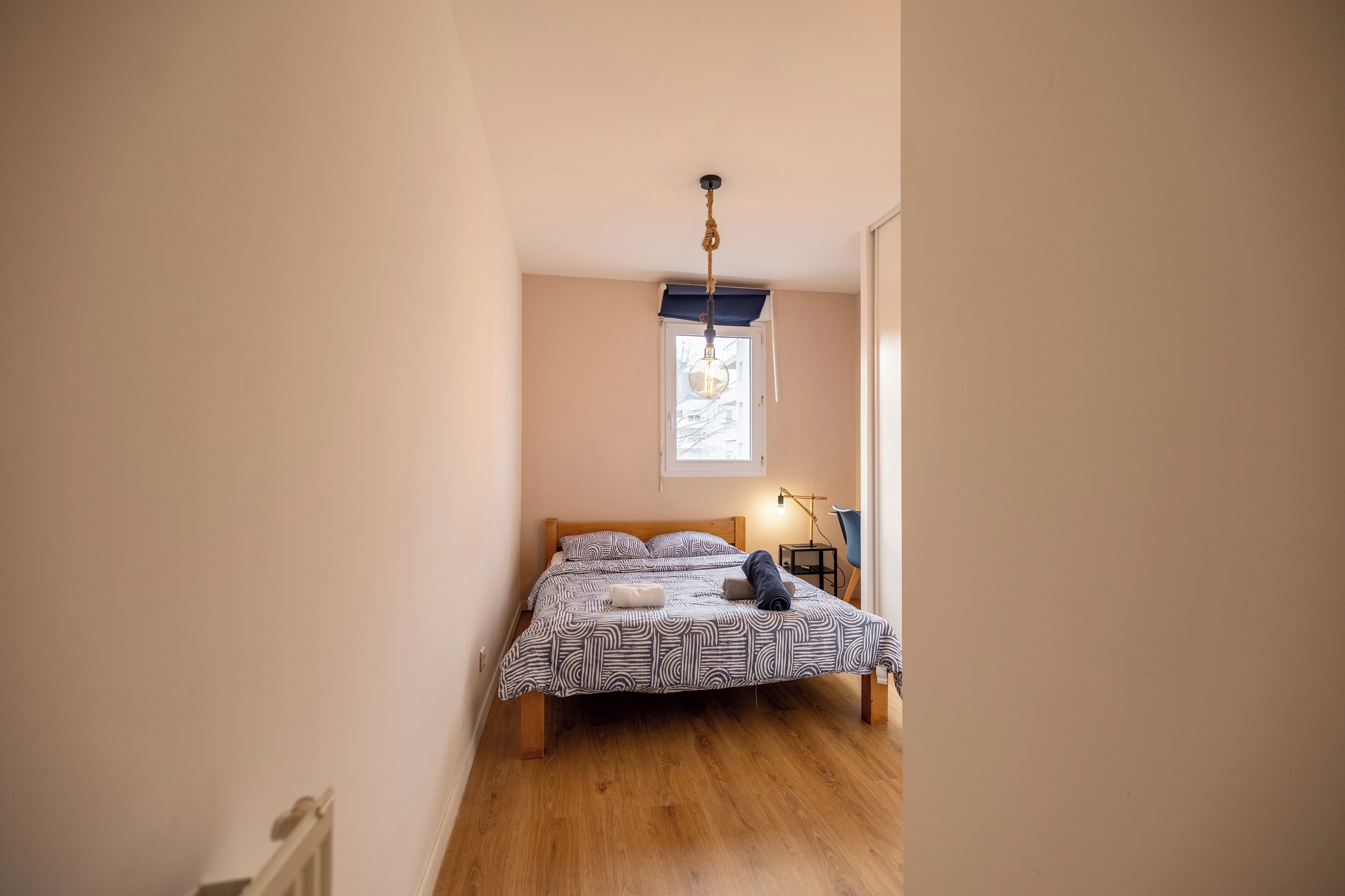 A bedroom with a bed, a window, a lamp, and a door.