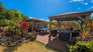 An outdoor patio area with a covered seating area, tables, and a barbecue grill. - Gods Peace Of Maui (Makawao)