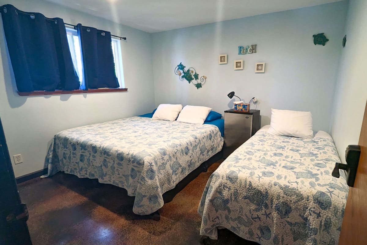 Ein Zimmer mit zwei Betten, einem kleinen Schreibtisch und einem Fenster mit Vorhängen.