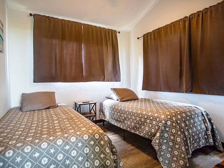 A room with two beds, brown curtains, patterned bedding, and a small table.