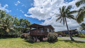 A wooden house with a balcony, surrounded by lush greenery and palm trees. - Gods Peace Of Maui (Makawao)