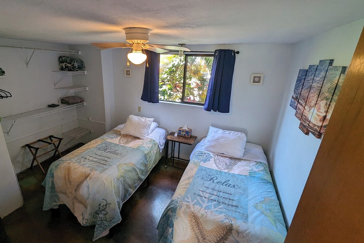 Ein kleines, sauberes Zimmer mit zwei Einzelbetten, einem Schreibtisch und einem Stuhl.