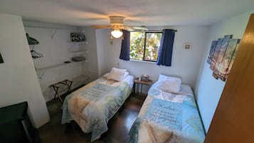 Ein kleines, sauberes Zimmer mit zwei Einzelbetten, einem Schreibtisch und einem Stuhl.