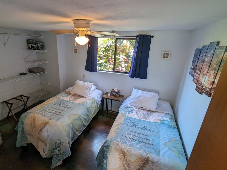 A small, clean room with two single beds, a desk, and a chair.