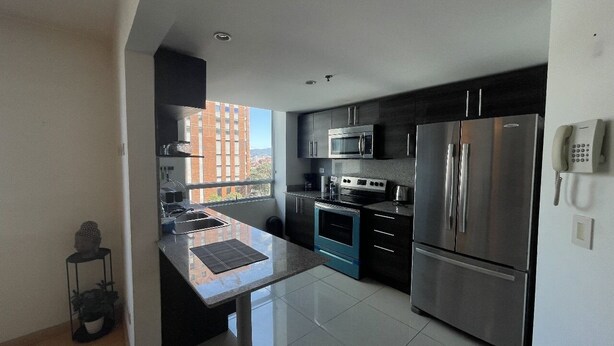 A modern kitchen with stainless steel appliances, a black countertop, and a view of a building outside.