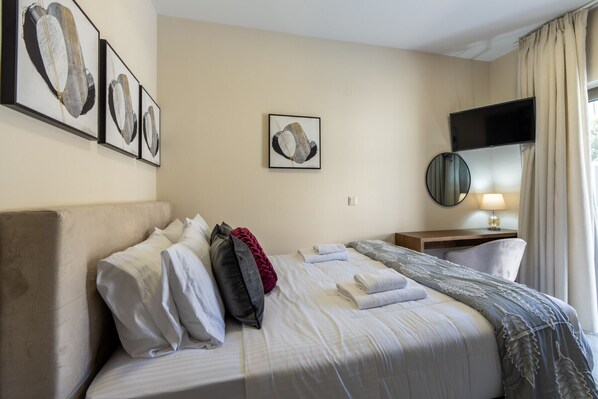 A hotel room with a bed, a desk, a TV, and artwork on the wall.