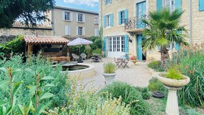 A courtyard with a fountain, outdoor seating, and a variety of plants. - Aux Berges du Libre (Félines-Termenès)