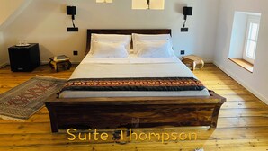 A bedroom with a large bed, two wall-mounted lamps, a small table, a rug, and a window with a view. - Aux Berges du Libre (Félines-Termenès)