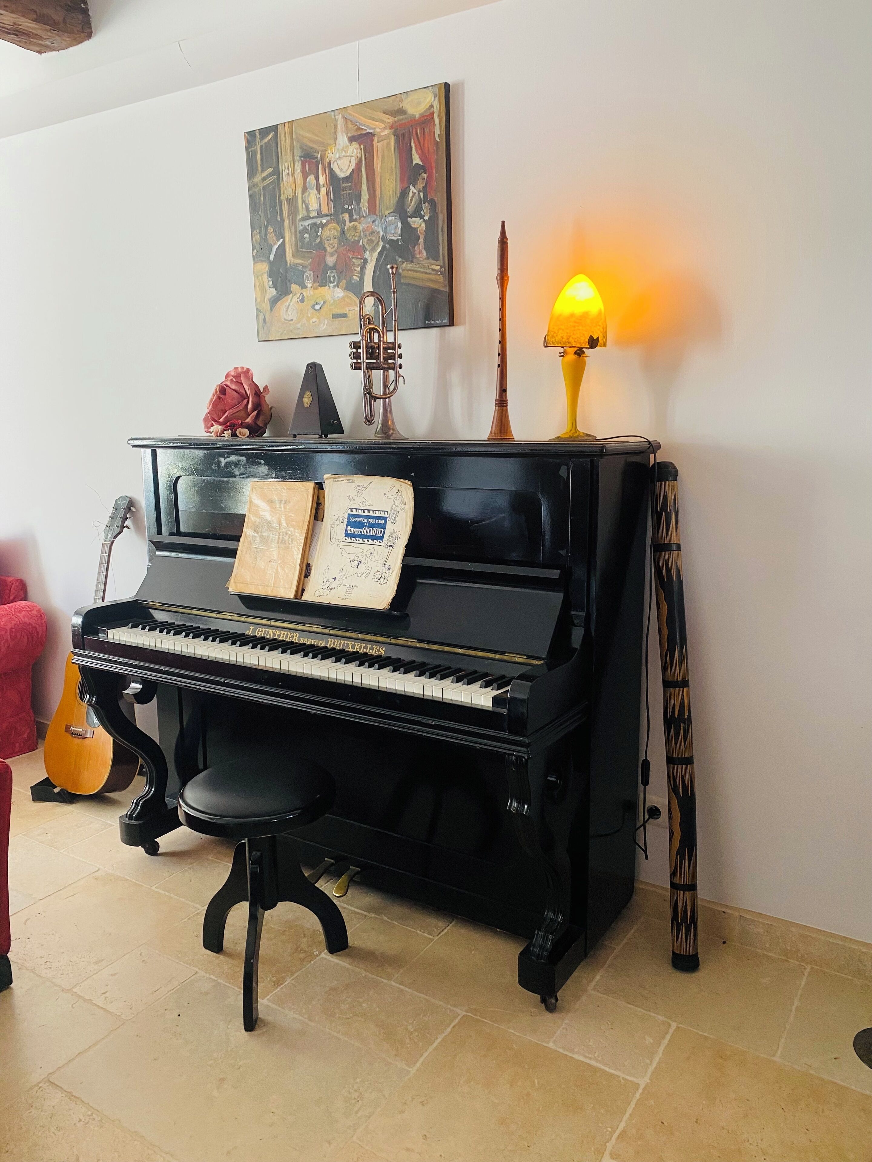 Ein schwarzes, stehendes Klavier mit Noten, eine Gitarre und eine dekorative Lampe in einem Raum mit Fliesenboden.