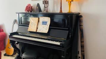 Ein schwarzes, stehendes Klavier mit Noten, eine Gitarre und eine dekorative Lampe in einem Raum mit Fliesenboden.