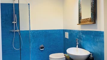 Un baño con ducha envuelta en vidrio, inodoro y lavamanos con espejo.