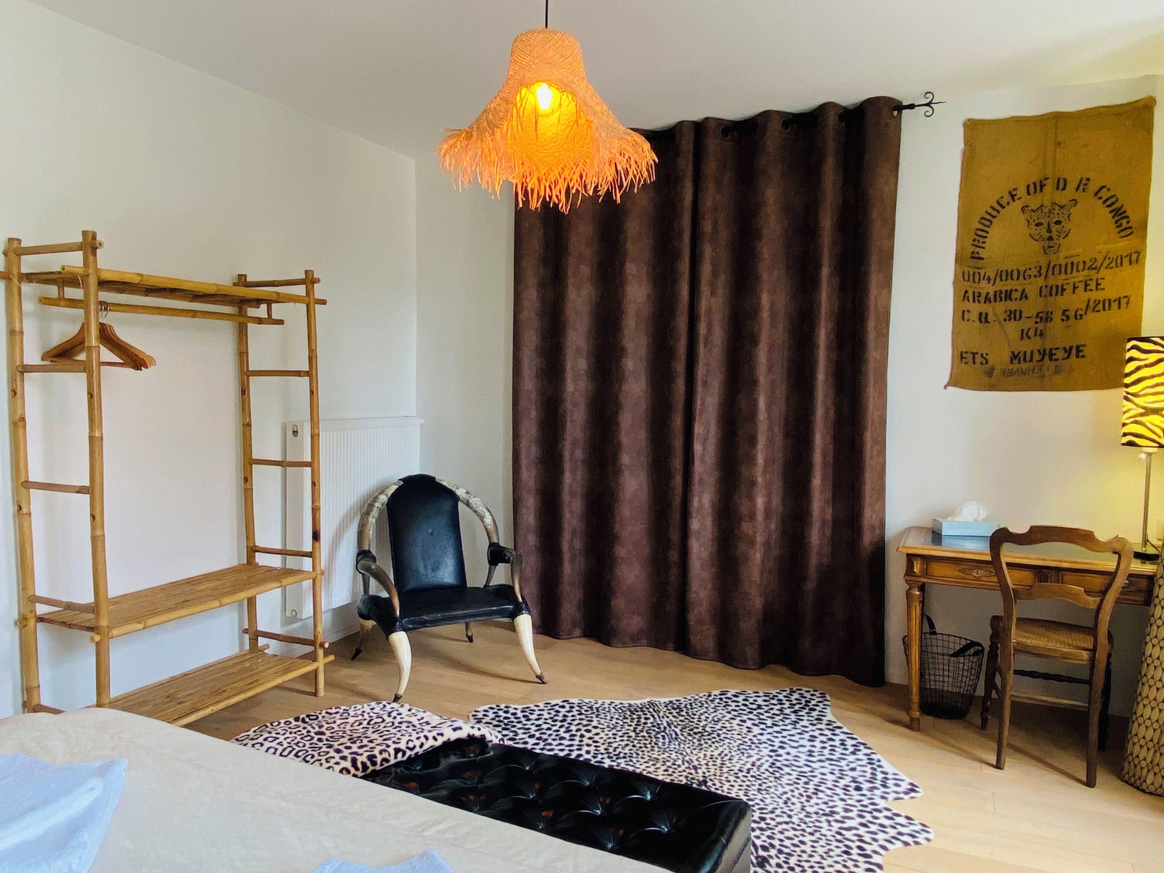 Una habitación con cama, una silla, un escritorio, una lámpara colgante, una escalera de madera y una cortina.