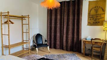 Una habitación con cama, una silla, un escritorio, una lámpara colgante, una escalera de madera y una cortina.