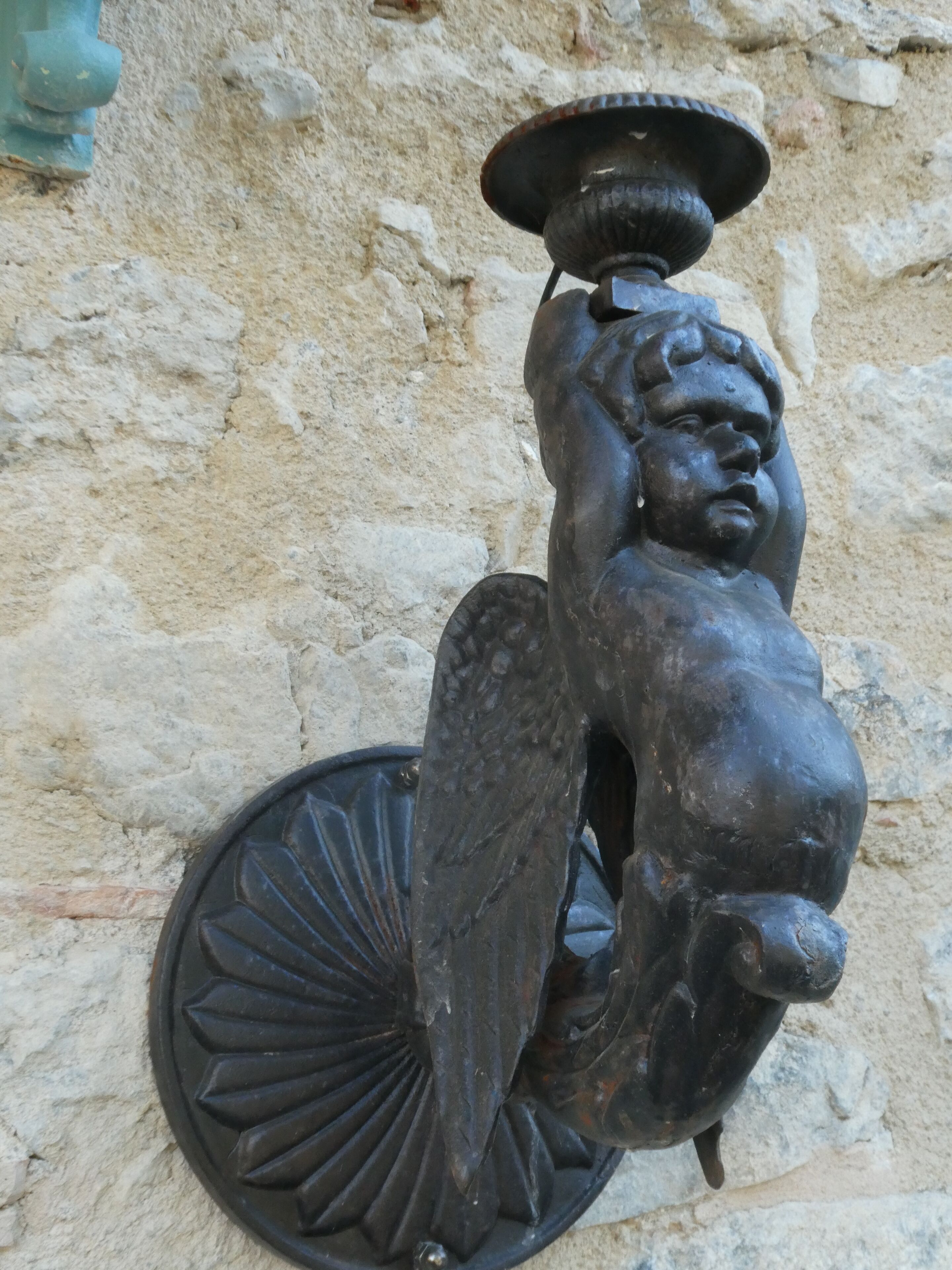 Escultura metàl·lica d'una figura que sosté un bol, subjecta a una paret amb relleu.