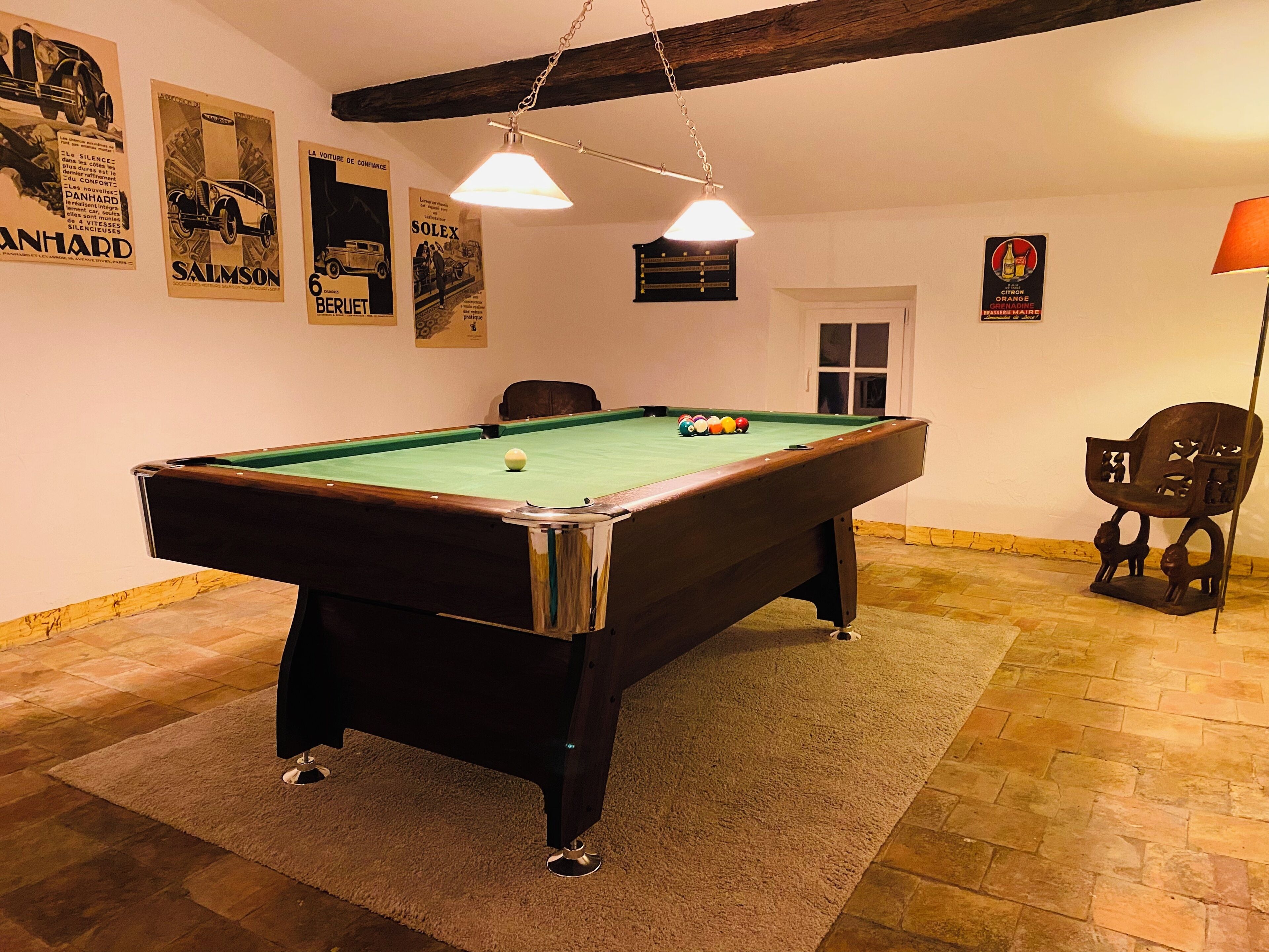Una mesa de billar en una habitación con techo de madera, una silla y una lámpara.