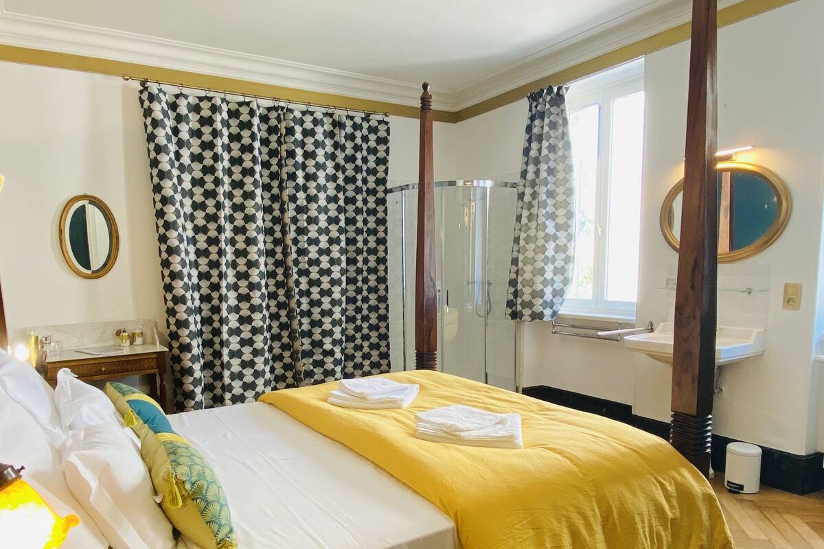 A hotel room with a bed, a bathroom with a mirror, and a window with curtains.