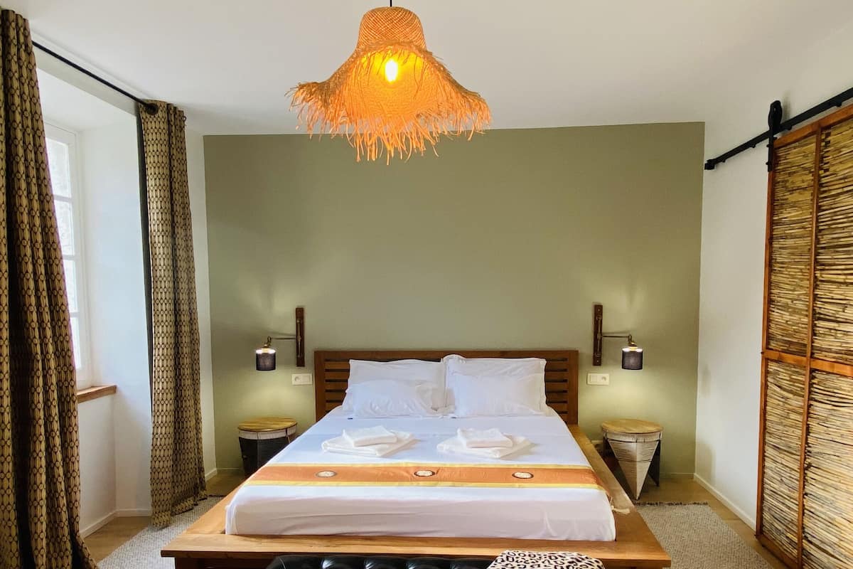 A hotel room with a large bed, two bedside tables, a hanging light fixture, and a wardrobe with a woven pattern.