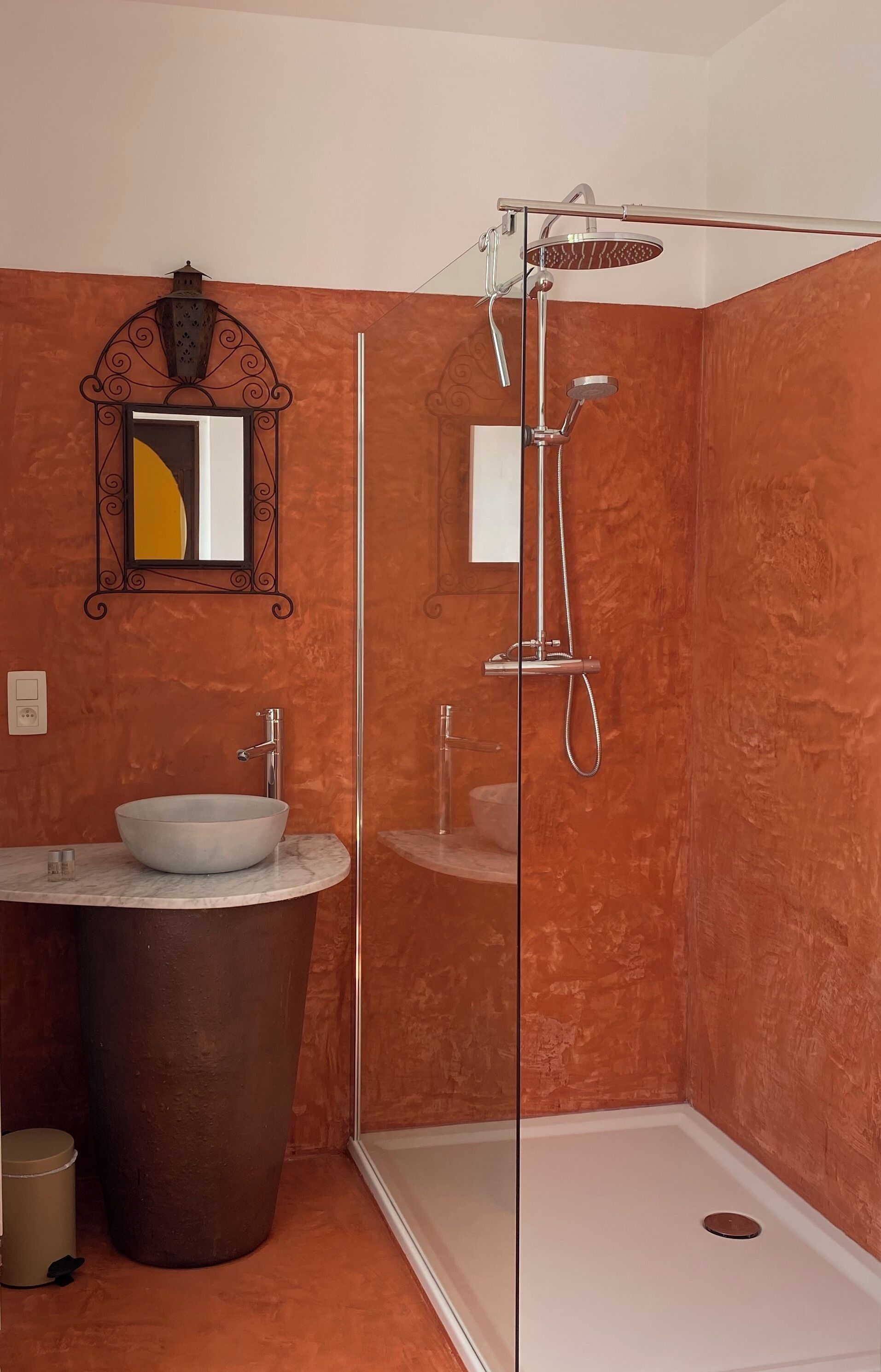 A bathroom with a glass-enclosed shower, a marble sink, and a large trash bin.
