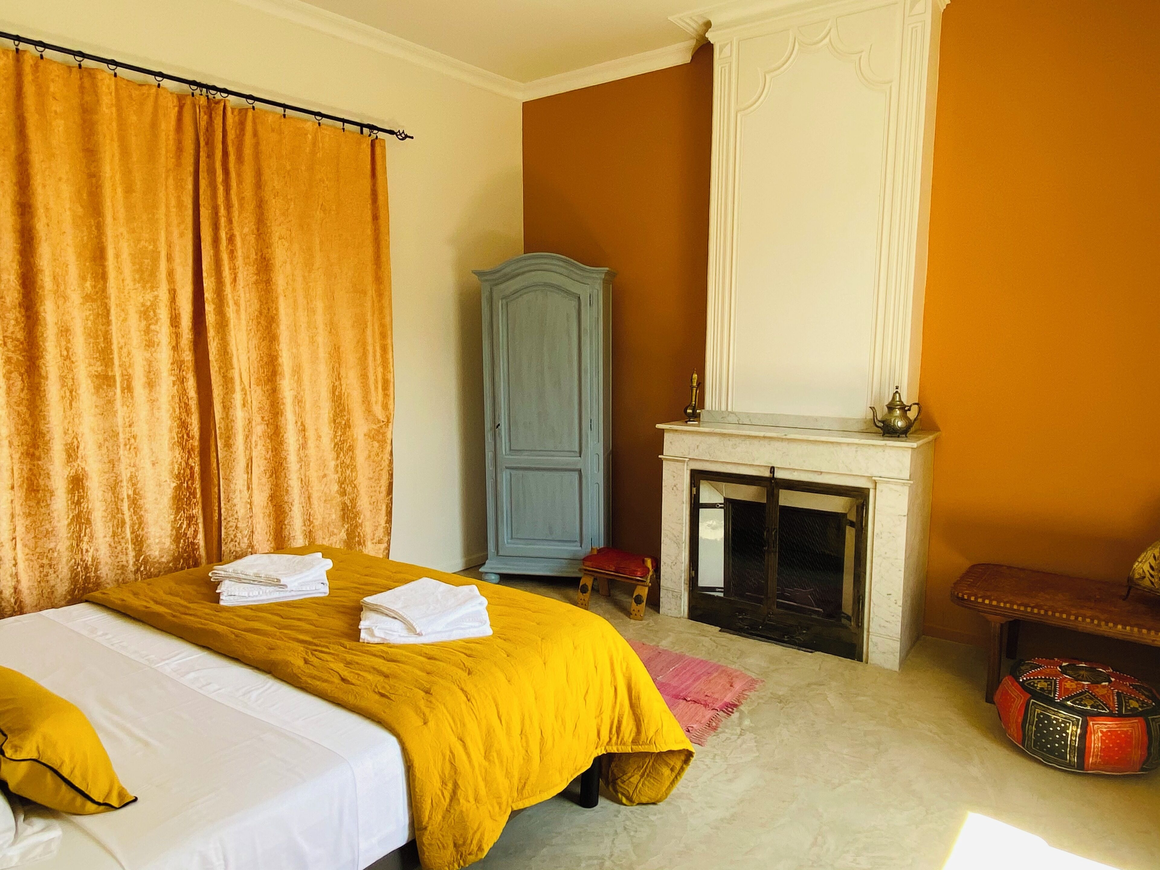Un dormitorio con cama, armario, chimenea y una mesita.