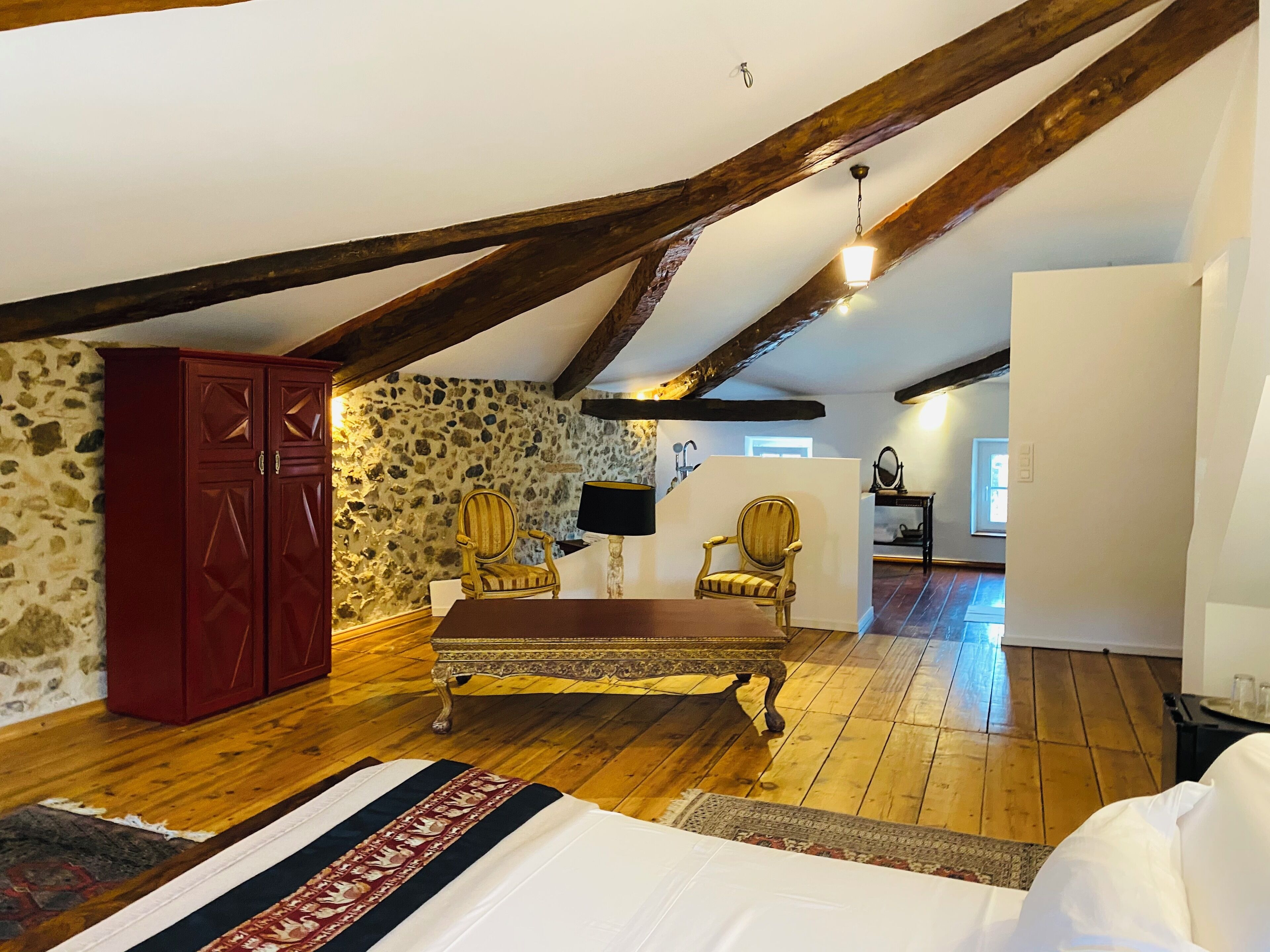 A room with a wooden floor, a bed, a stone wall, and a wooden ceiling beam.