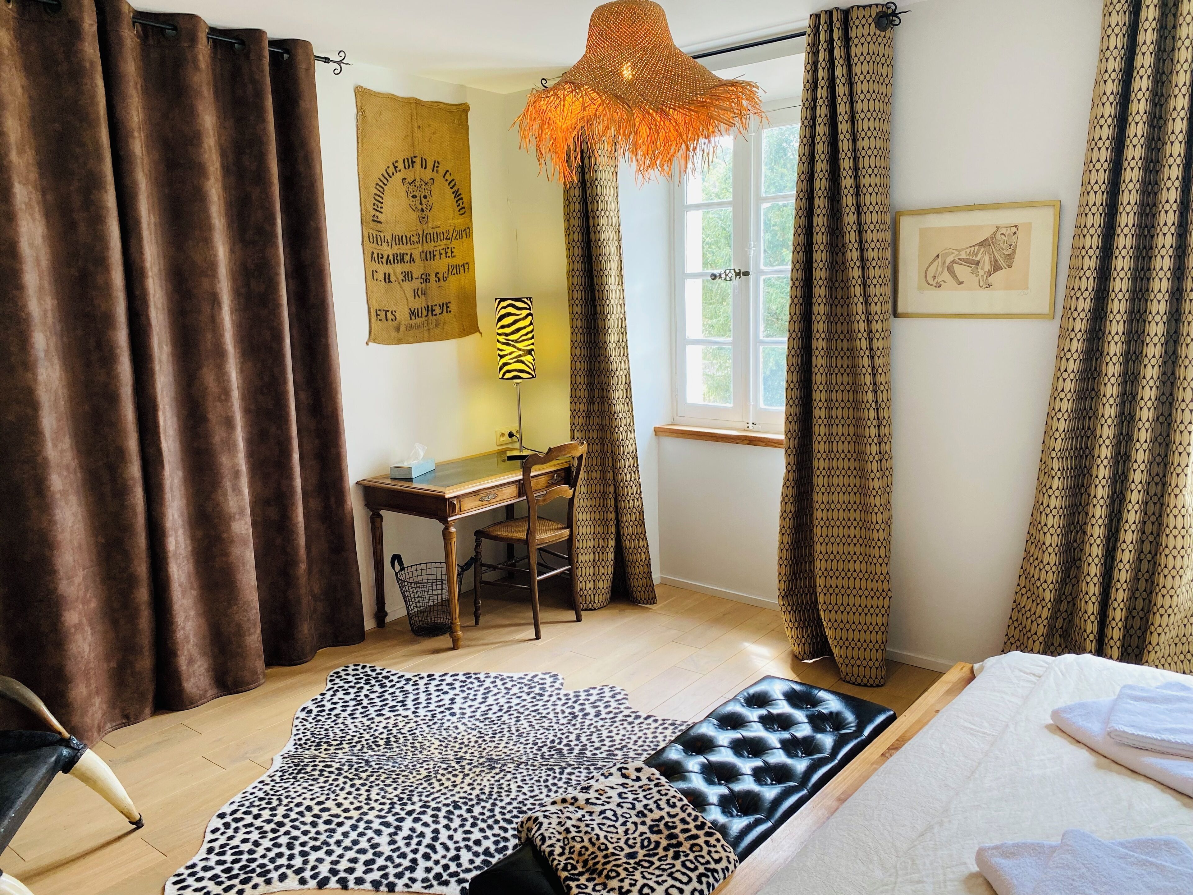 Una habitación con escritorio, silla y cama con colcha de estampado de leopardo. Hay una ventana con cortinas y un adorno en la pared.