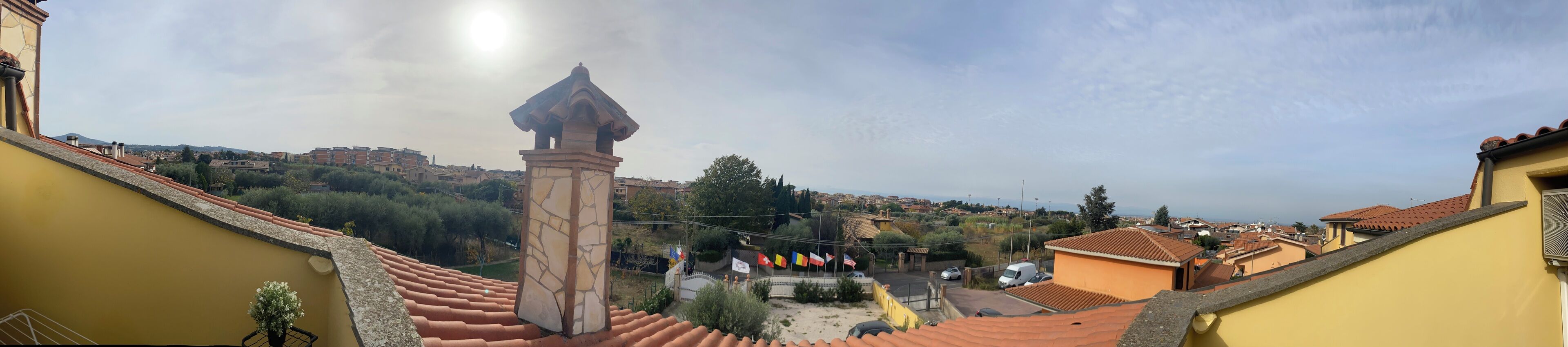 A view from a balcony overlooking a residential area with terracotta roofs, a stone pillar, and a clear sky.