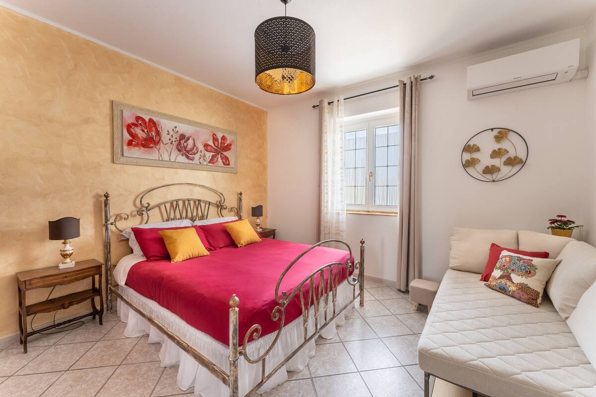 A bedroom with a bed, bedside tables, a sofa, a window with curtains, and wall decorations.
