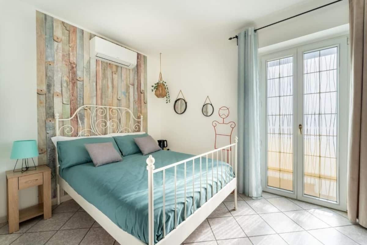 A bedroom with a bed, a nightstand, a wall-mounted air conditioner, and a window with curtains.
