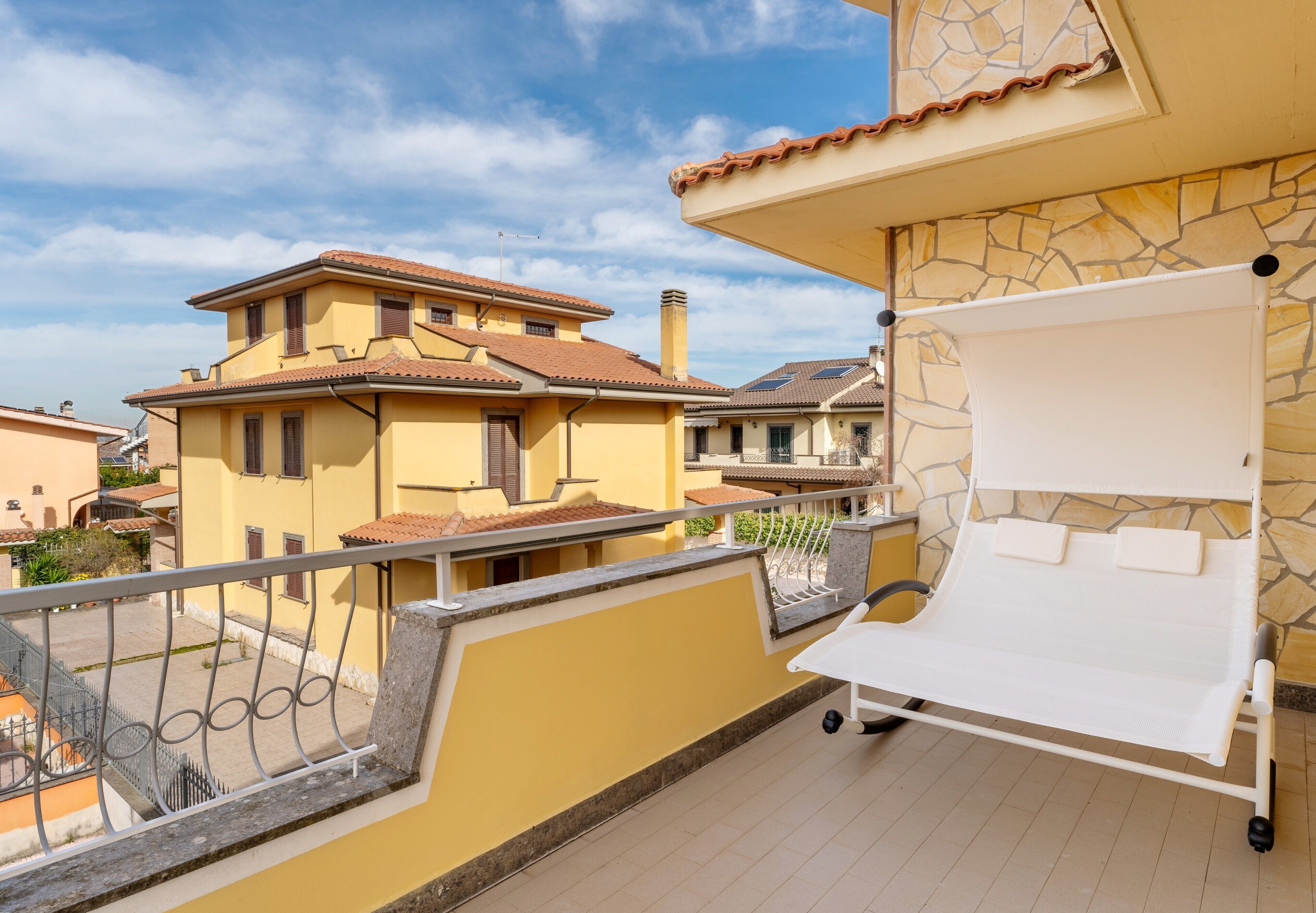 Un balcon avec un transat blanc, un mur en pierre et une vue sur les bâtiments voisins.