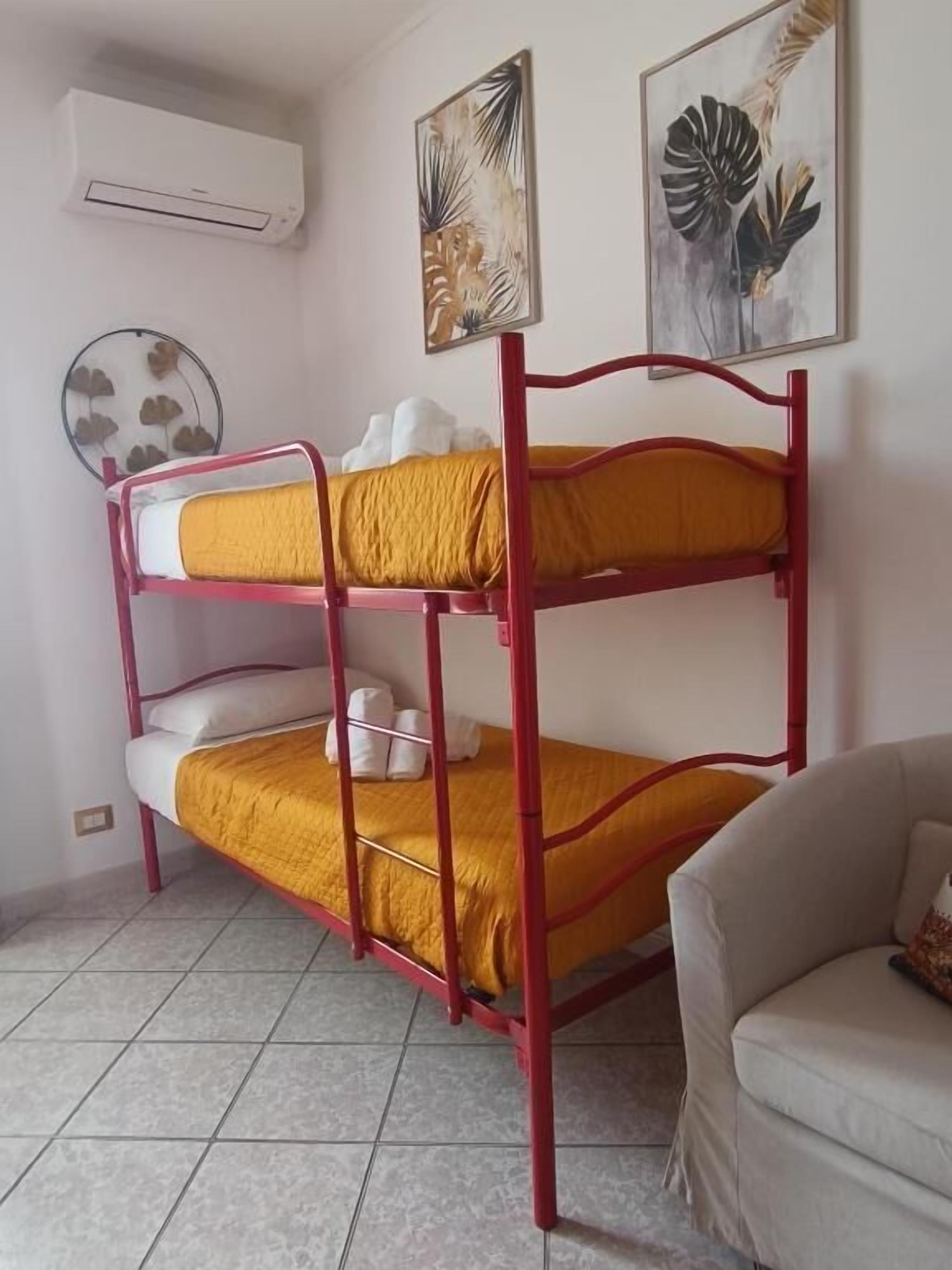 A bunk bed with yellow bedding, a white air conditioner, and two framed botanical prints on the wall.