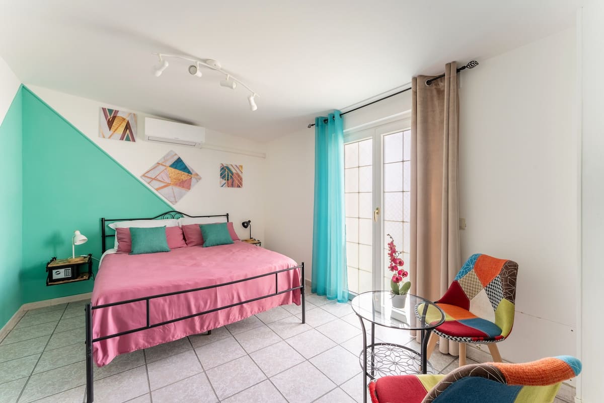 A bedroom with a bed, a chair, a small table, and a window with curtains.